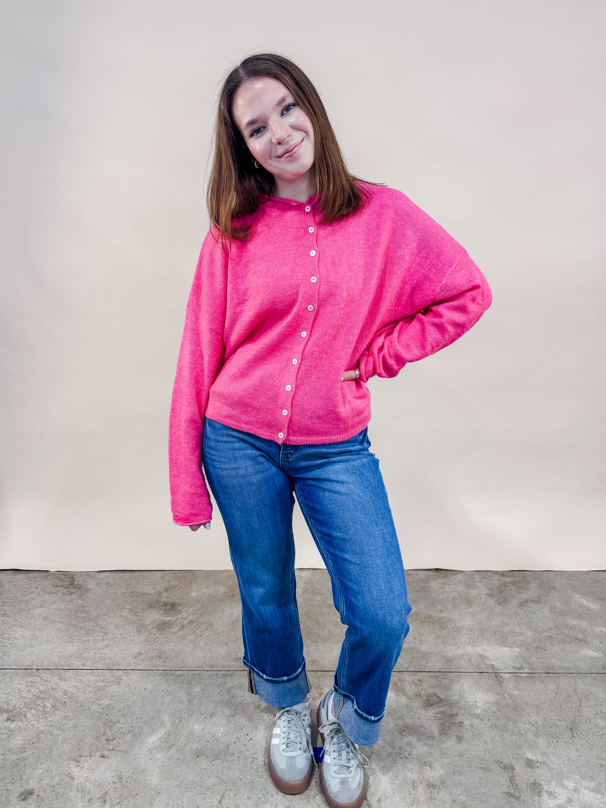 Woman wearing a bright pink cardigan and cuffed straight leg jeans.