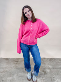 Woman wearing a bright pink cardigan and cuffed straight leg jeans.