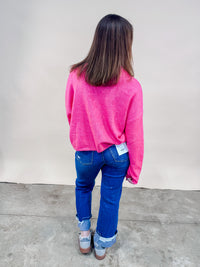 Back of woman wearing bright pink cardigan and cuffed straight leg jeans. 