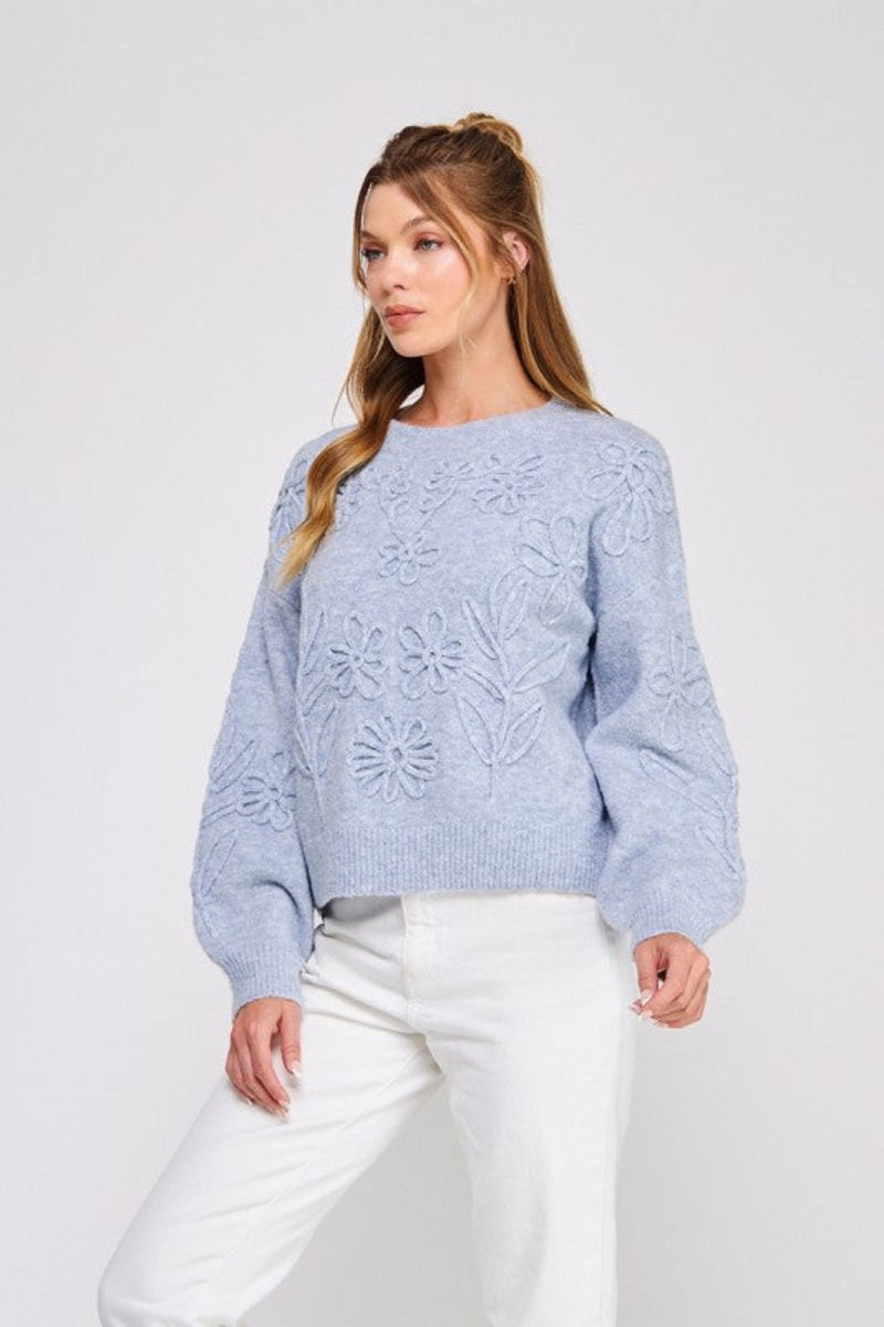 Woman wearing a light blue sweater with floral patterns on a white background