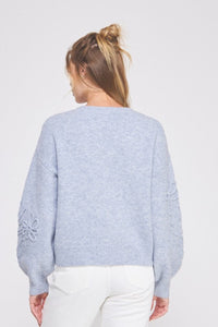 Woman wearing a light blue sweater with floral details on a white background