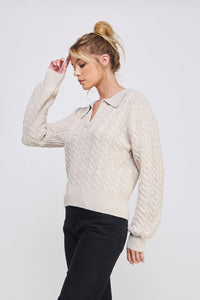 Woman wearing a cream cable knit sweater against a white background