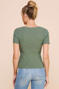 Person wearing a green ribbed sweater and blue jeans on a beige background