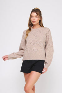 Woman wearing a beige sweater with floral patterns on a white background