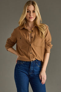 Woman wearing a brown shirt and blue jeans against a gray background