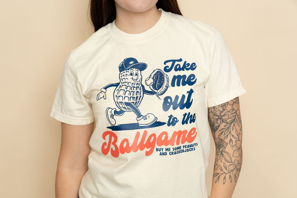 Ivory baseball graphic tee with “Take Me Out to the Ball Game” design, casual boutique t-shirt for everyday style.
