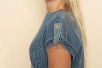 Closeup view of blue knit short sleeve sweater with button details. 