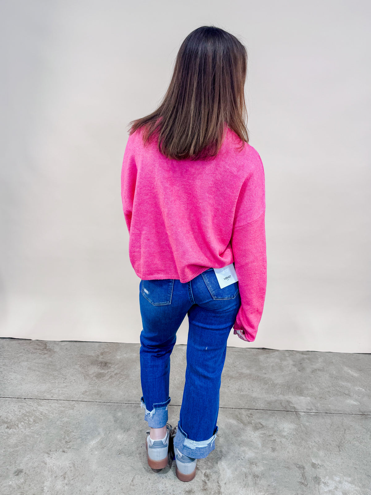 Back of woman wearing bright pink cardigan and cuffed straight leg jeans. 