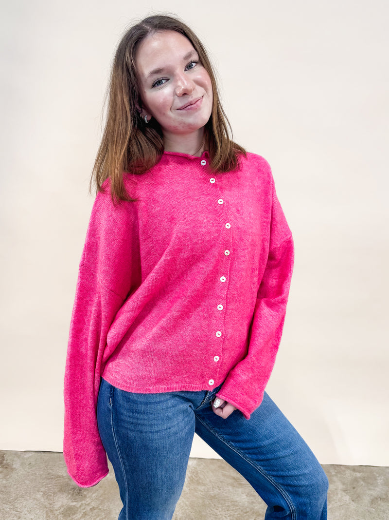 Woman wearing a bright pink Piper cardigan with buttons and blue jeans for a cute casual outfit. 