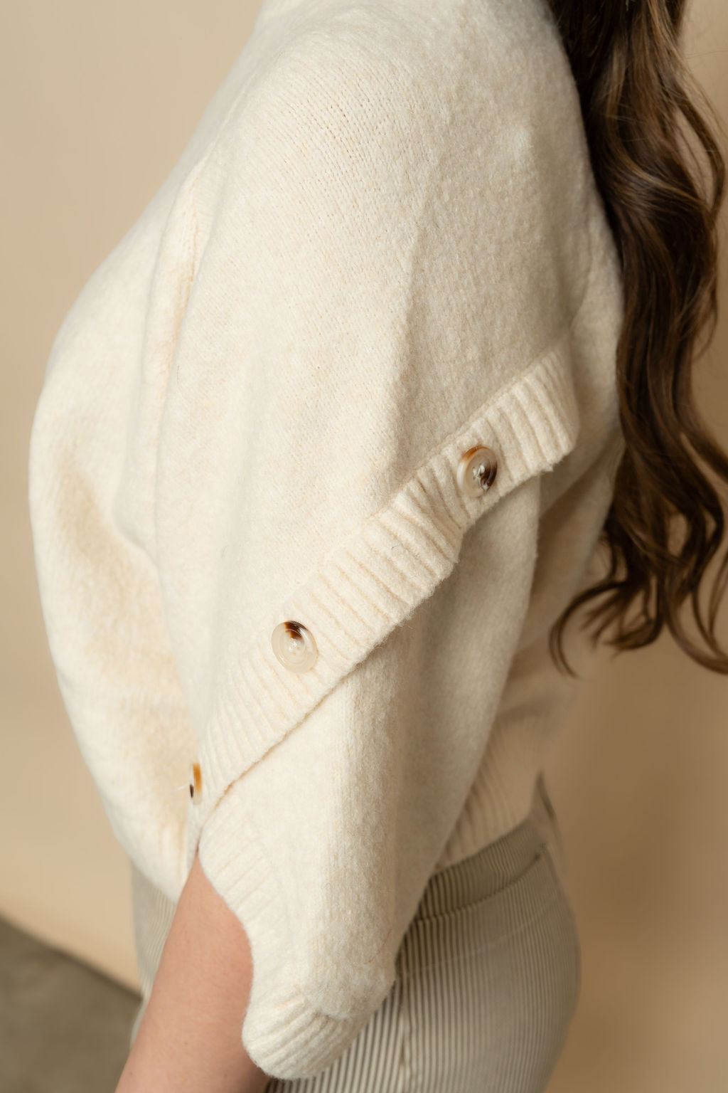 Closeup of buttons on short sleeve cream knit sweater for women. 