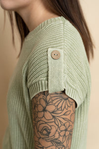 Closeup of button detail on sage green knit short sleeve sweater for women. 