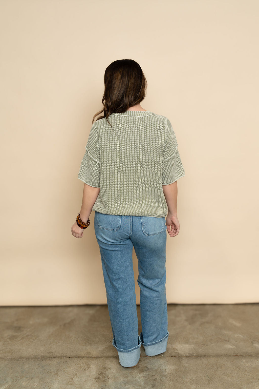 Back view of sage knit short sleeve sweater paired with light wash denim for a cute spring outfit for women. 
