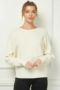 Woman wearing a cream sweater against a white wall