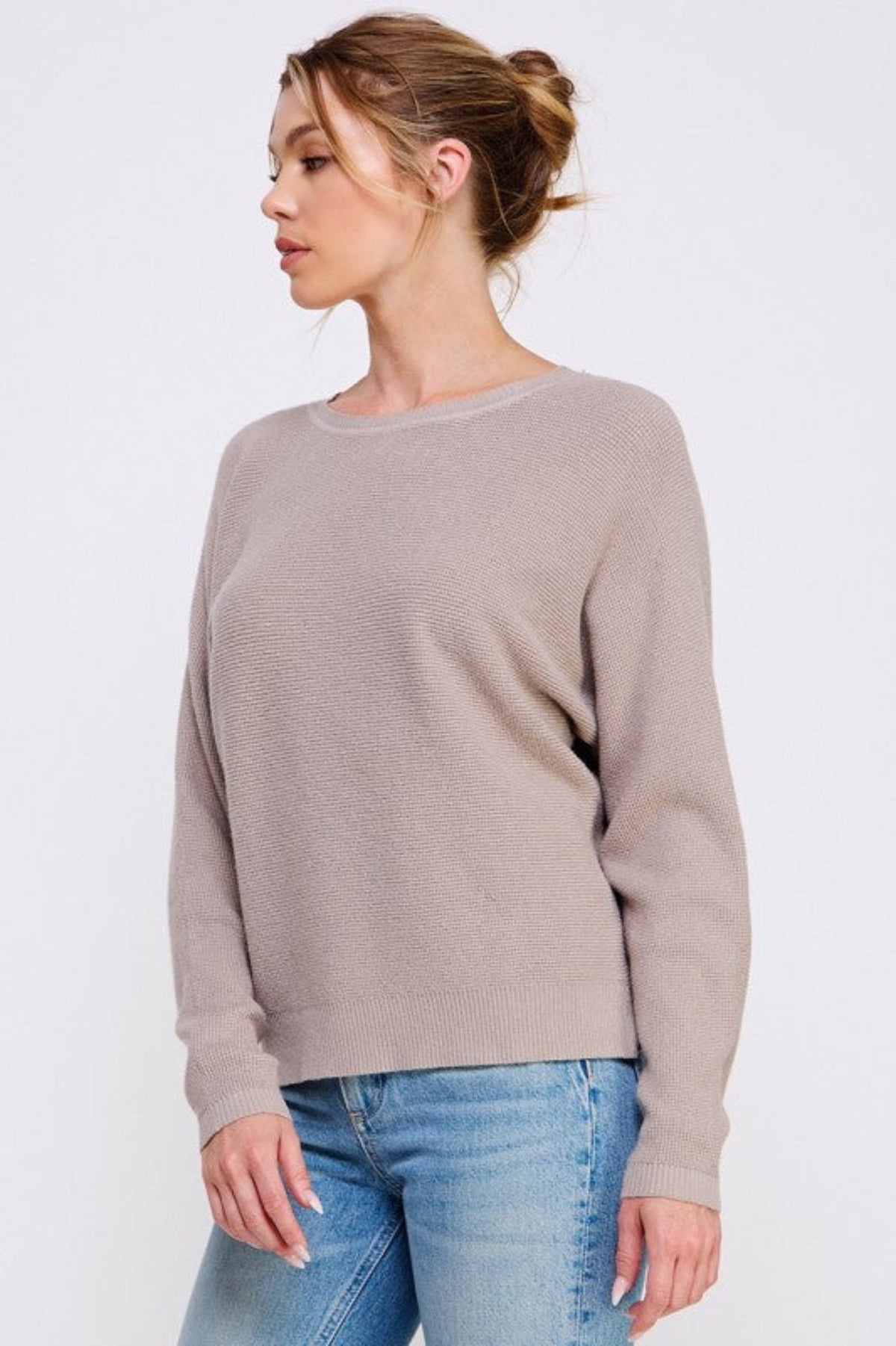 Woman wearing a beige sweater and blue jeans on a white background